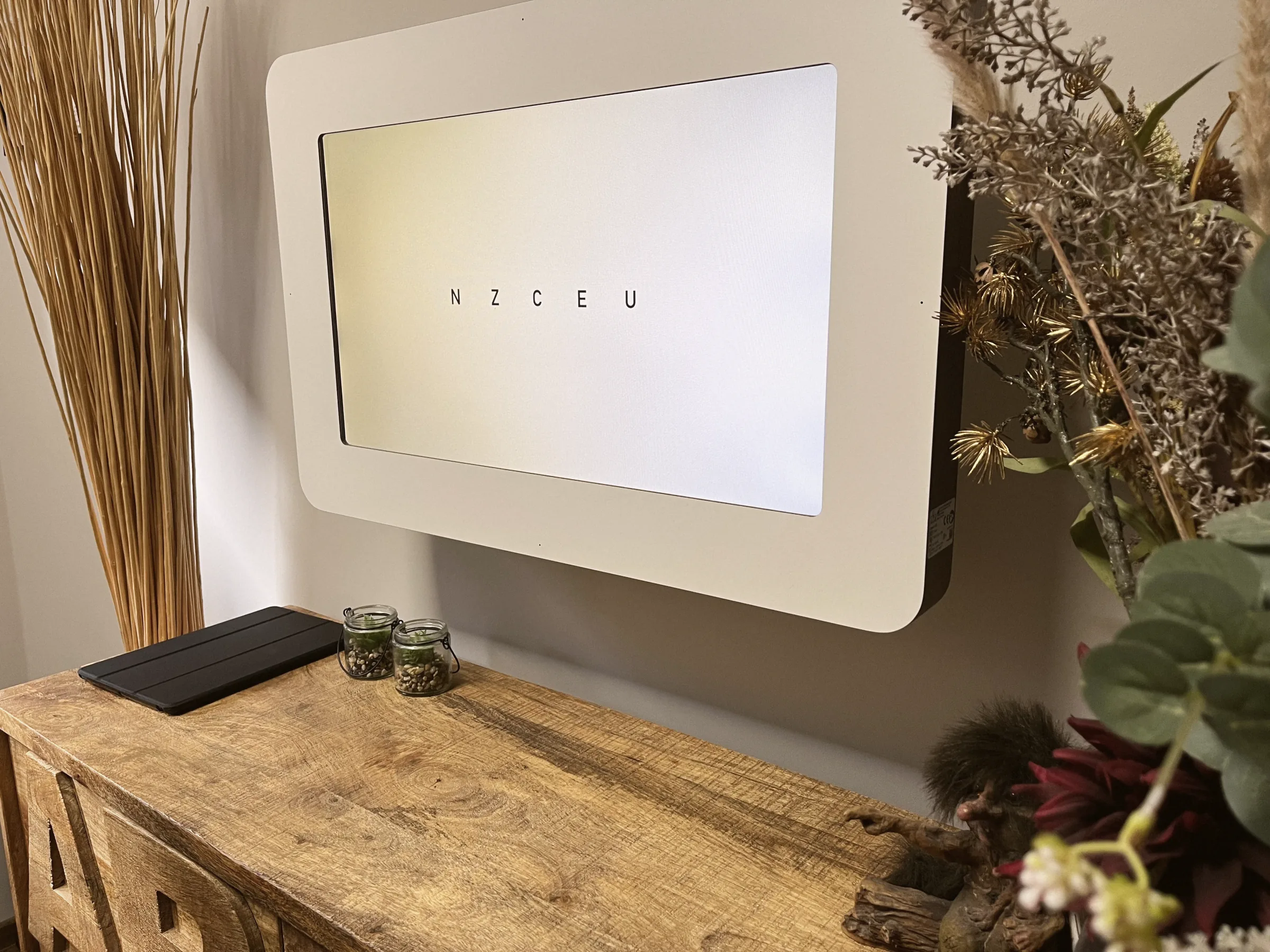 Ein Bildschirm mit Sehzeichen für den Sehtest hängt an der Wand über einer Holzkommode mit Trockenblumen.
